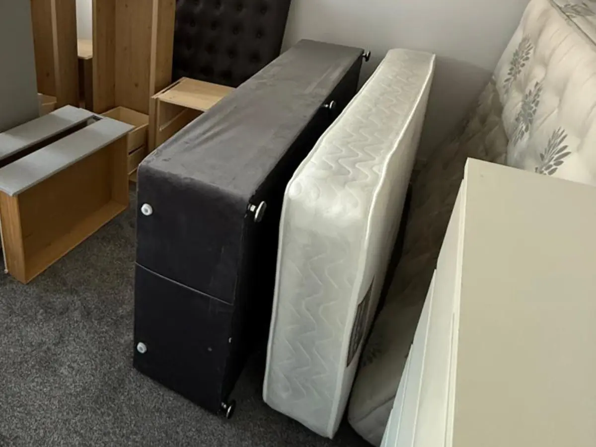 Old mattress and bed base stored indoors ready for collection, recycling, or responsible mattress disposal.