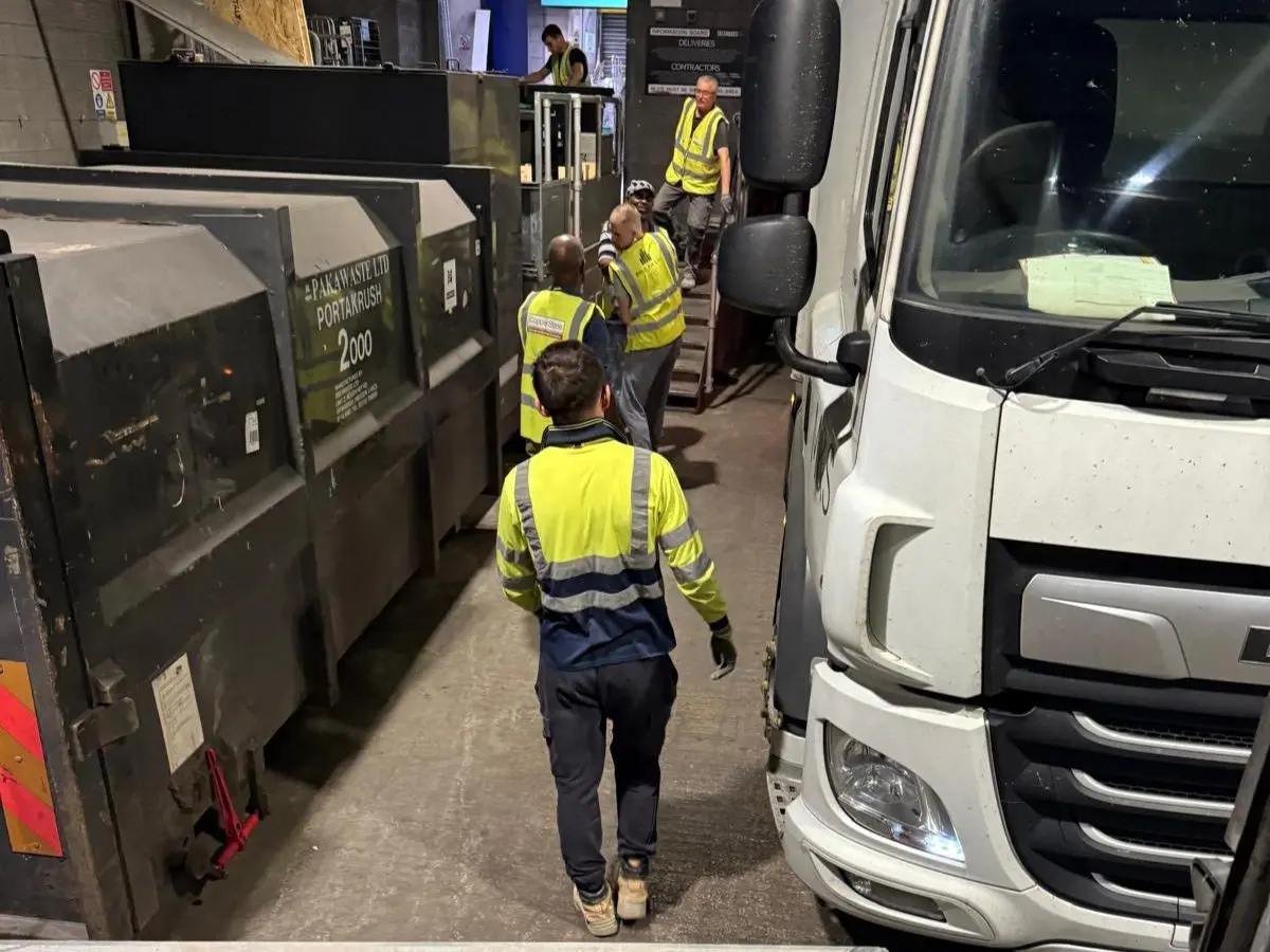 Waste collection team working beside commercial waste containers and collection vehicle during business waste removal operations.