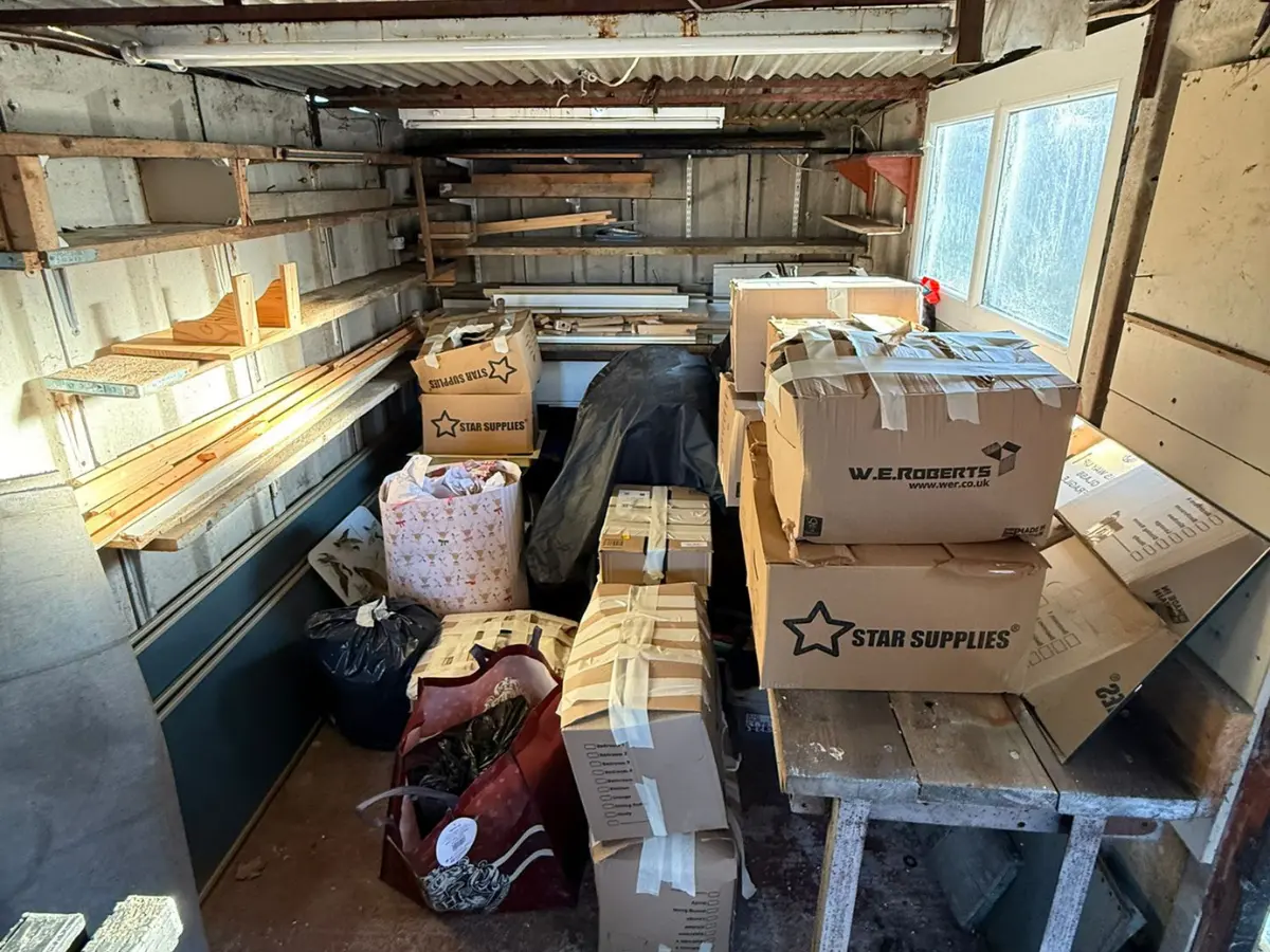 Packed storage shed with shelves, cardboard boxes and stored items ready for sorting and inventory before clearance.