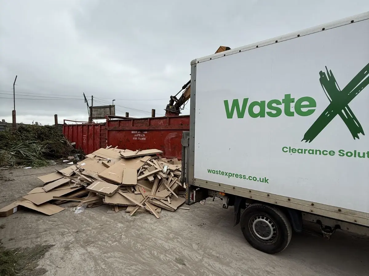 WasteXpress clearance vehicle beside a large pile of cardboard and timber waste at a commercial recycling facility.